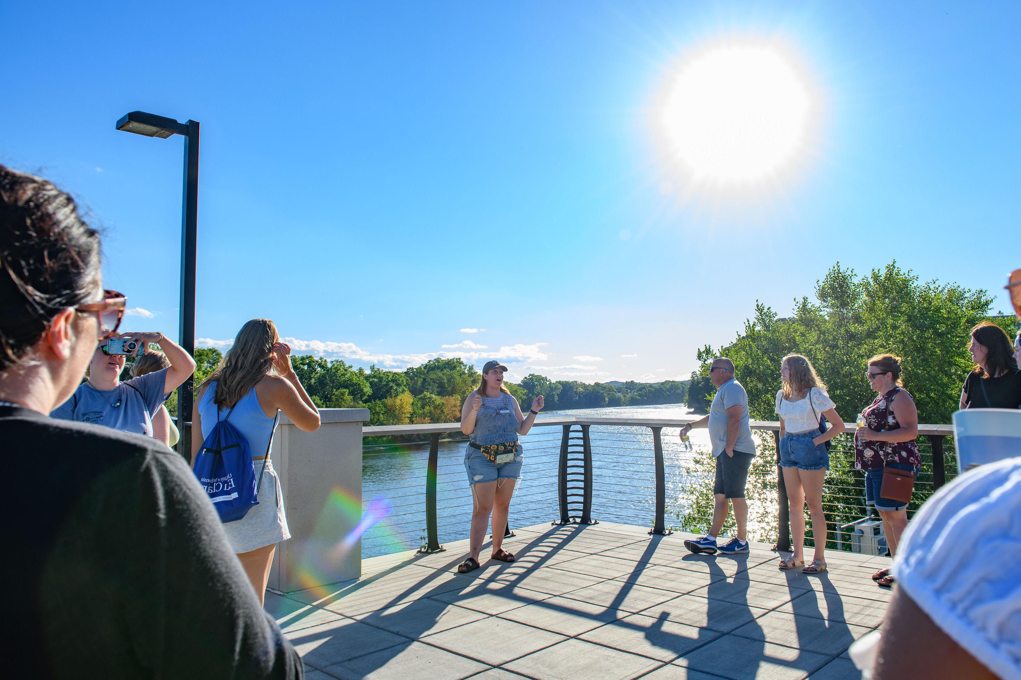 Campus visitors listen to a tour guide near the river during a sunny Sunset campus visit.