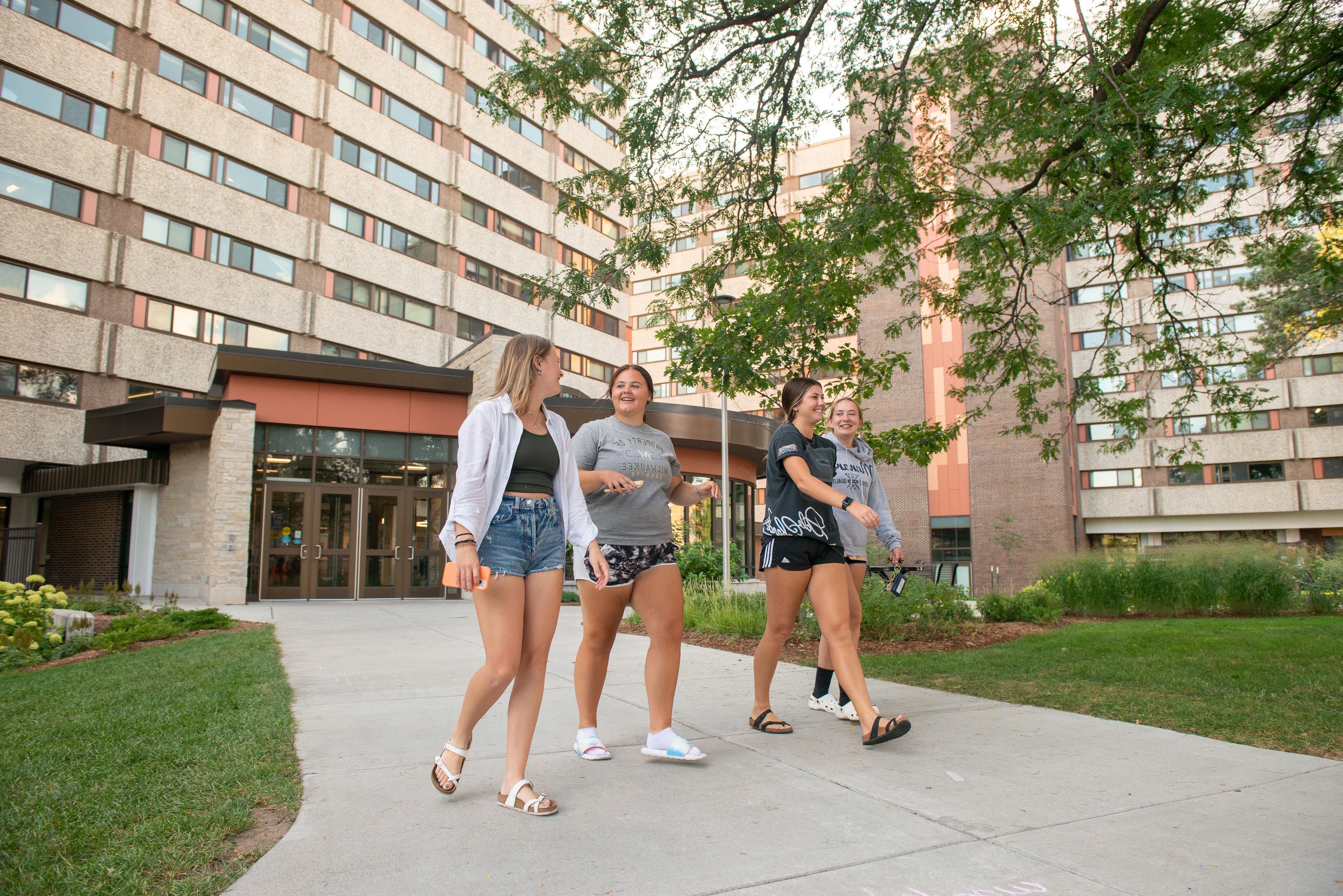 Students laughing and walking on 的 sidewalk on upper campus near Karlgaard Towers entrance.