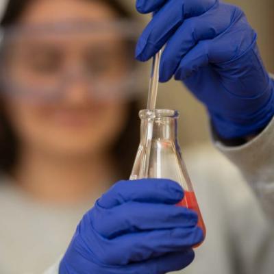 BioMed lab student holding a beaker, blue gloves 