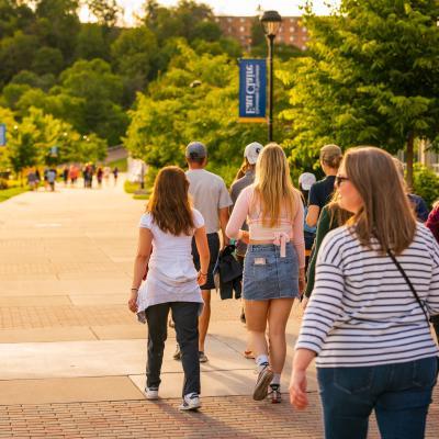 Campus visitors walk on the path towards the hill alongside the river during a campus tour.